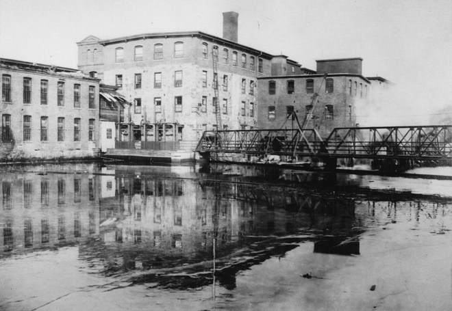 This photo just upstream from the dam and the former pedestrian bridge shows one of the mill buildings being demolished in the mid- 20th Century.